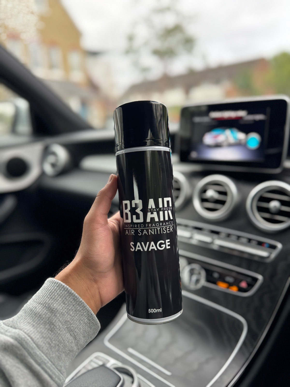Hand holding B3 AIR Savage air freshener spray inside a car