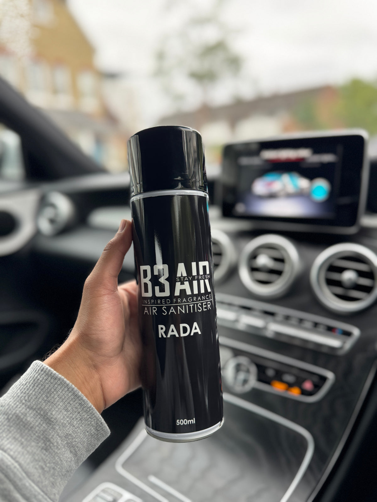 Hand holding B3 AIR Rada air freshener spray inside a car