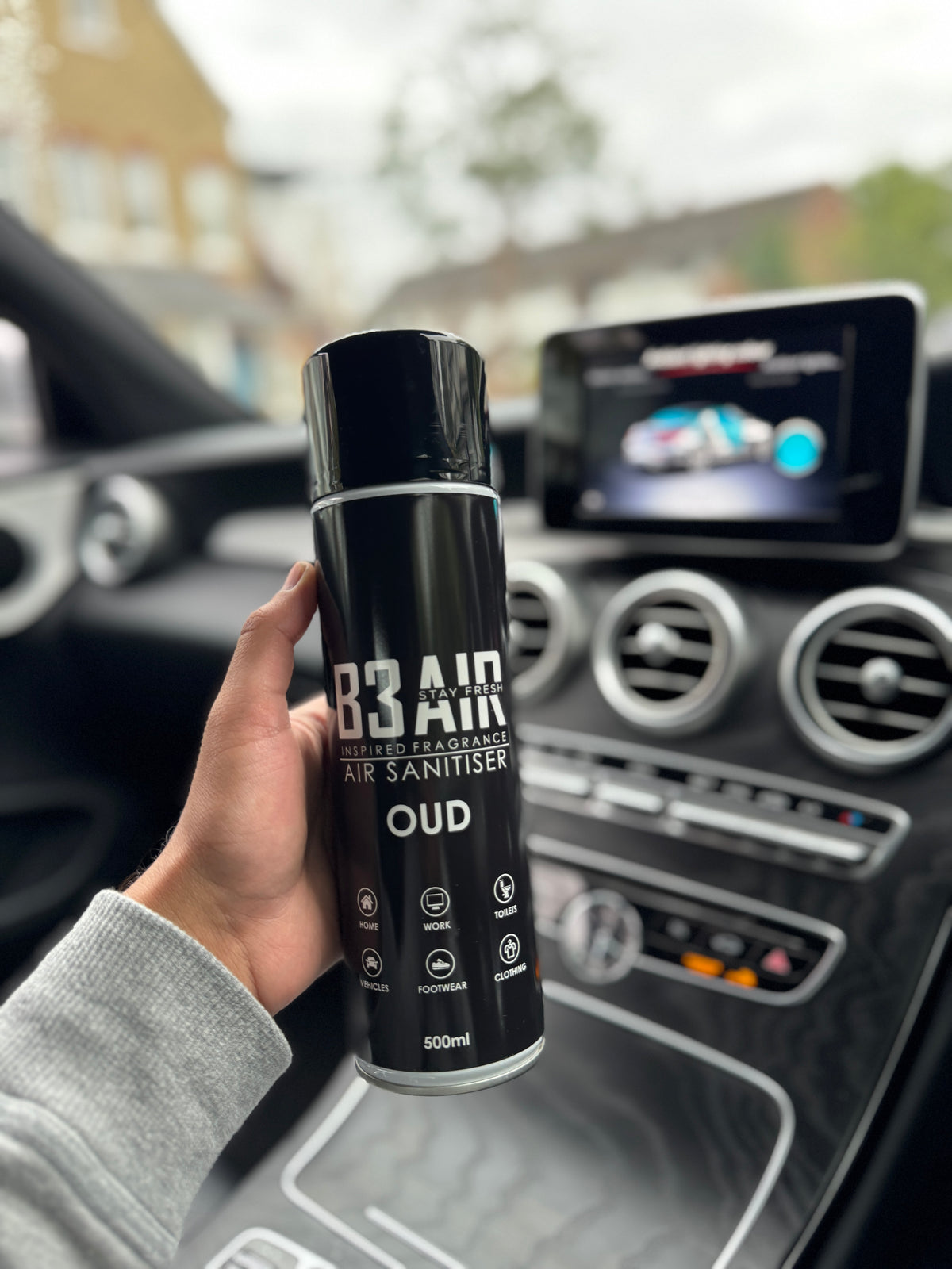 Hand holding B3 AIR Oud air freshener spray inside a car